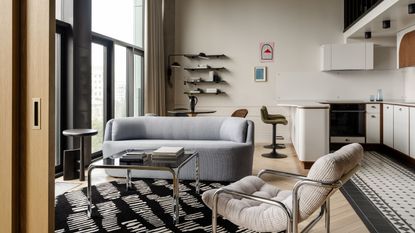 A spacious living room with white walls, a black and white rug, and gray furniture.