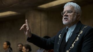 A bearded, white-haired man delivers an impassioned speech