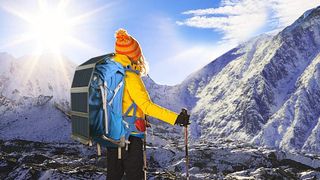 Woman in climbing gear looking at bright sun shining over mountain range, with one of the best solar chargers on her backpack