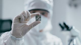 A technician inspects a chip in a semiconductor factory, holding it up to the camera