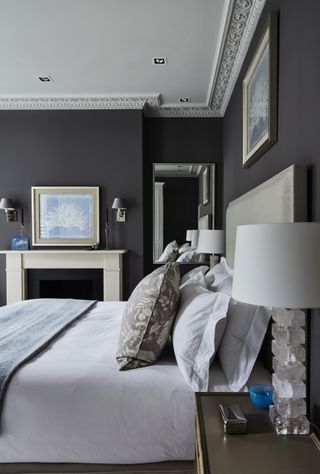 black and white bedroom, black walls, white ceiling, white bedlinen, wall lights, blue bedspread, taupe floral bed pillow, upholstered bed, artwork
