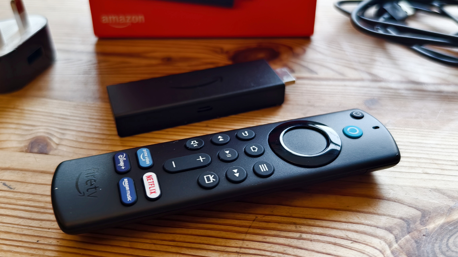 The Amazon Fire TV Stick next to its remote and box on a wooden table.