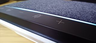 A grey, black and white Poly Sync 10 speakerphone sitting on a brown wooden desk