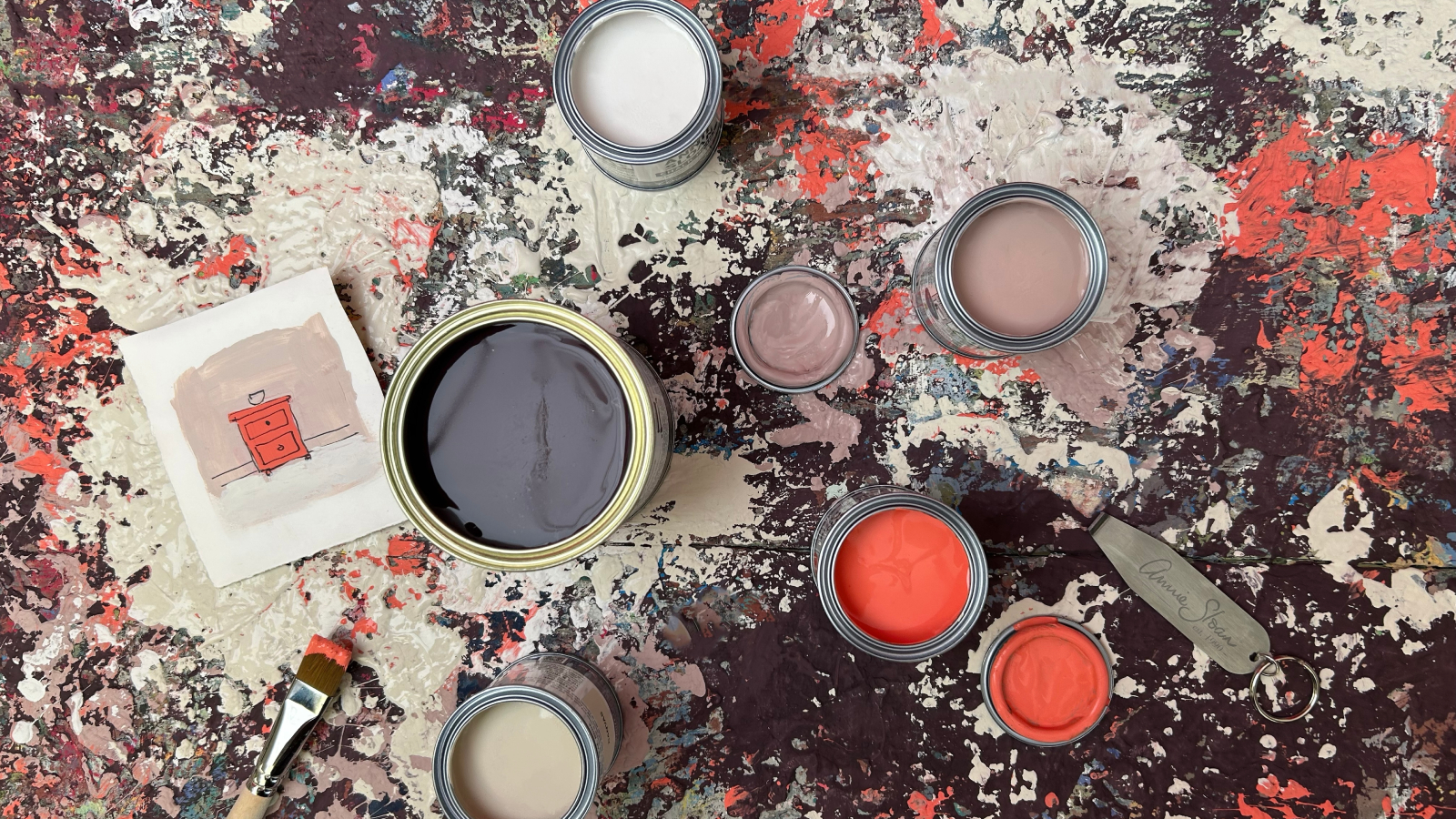 tins of paint open on surface covered with paint splashes and a piece of paper with sketch of painted side table