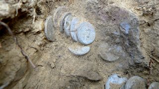 Here we see about 10 round silver coins half buried in the dirt. 