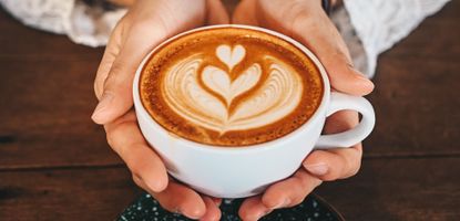 Cropped shot of woman hands holding a cup of hot latte coffee in her hands