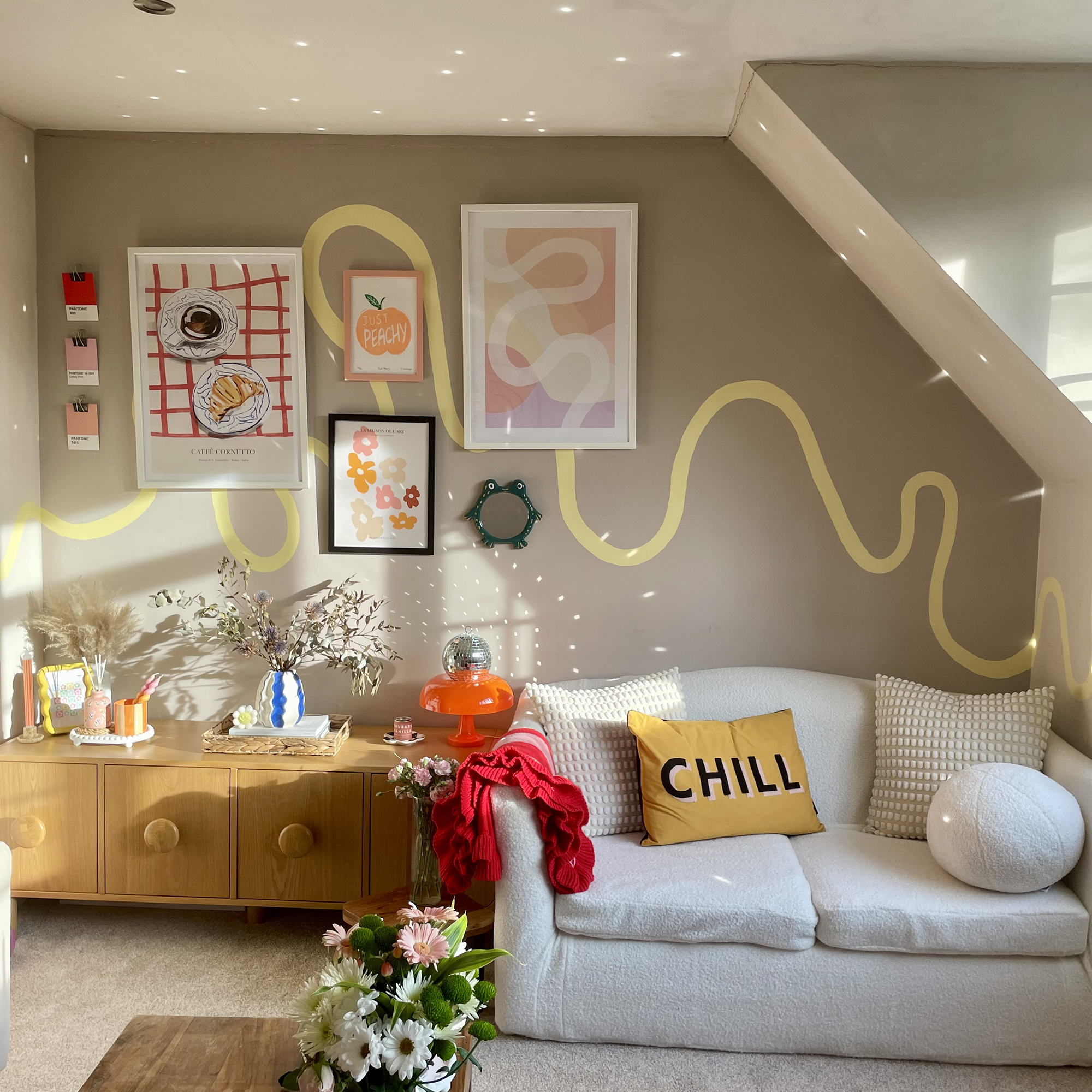 Eclectic living room with dark beige wall and a yellow-painted stripe running across it. Framed art hangs on the wall above a vintage sideboard and white sofa