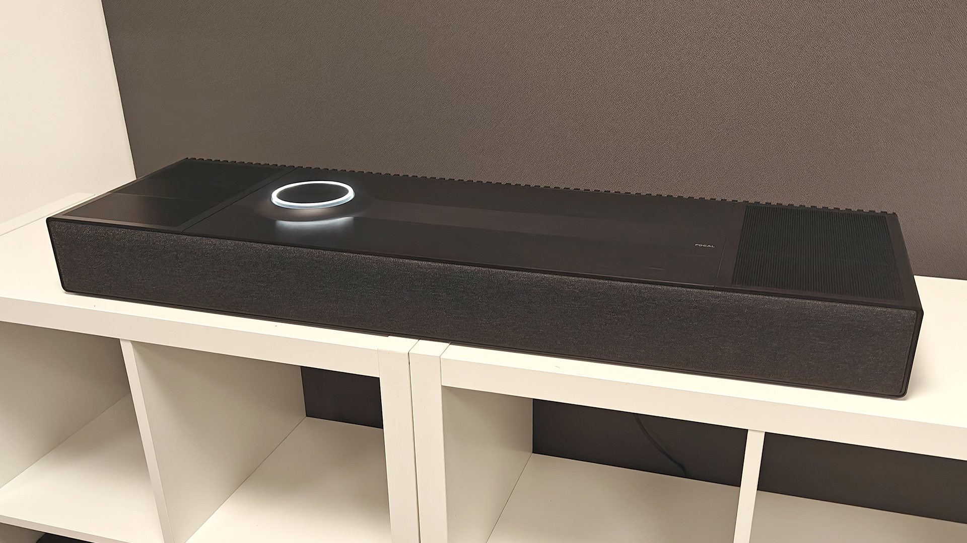 Focal Mu-so Hekla soundbar on white shelving unit in front of grey baffle