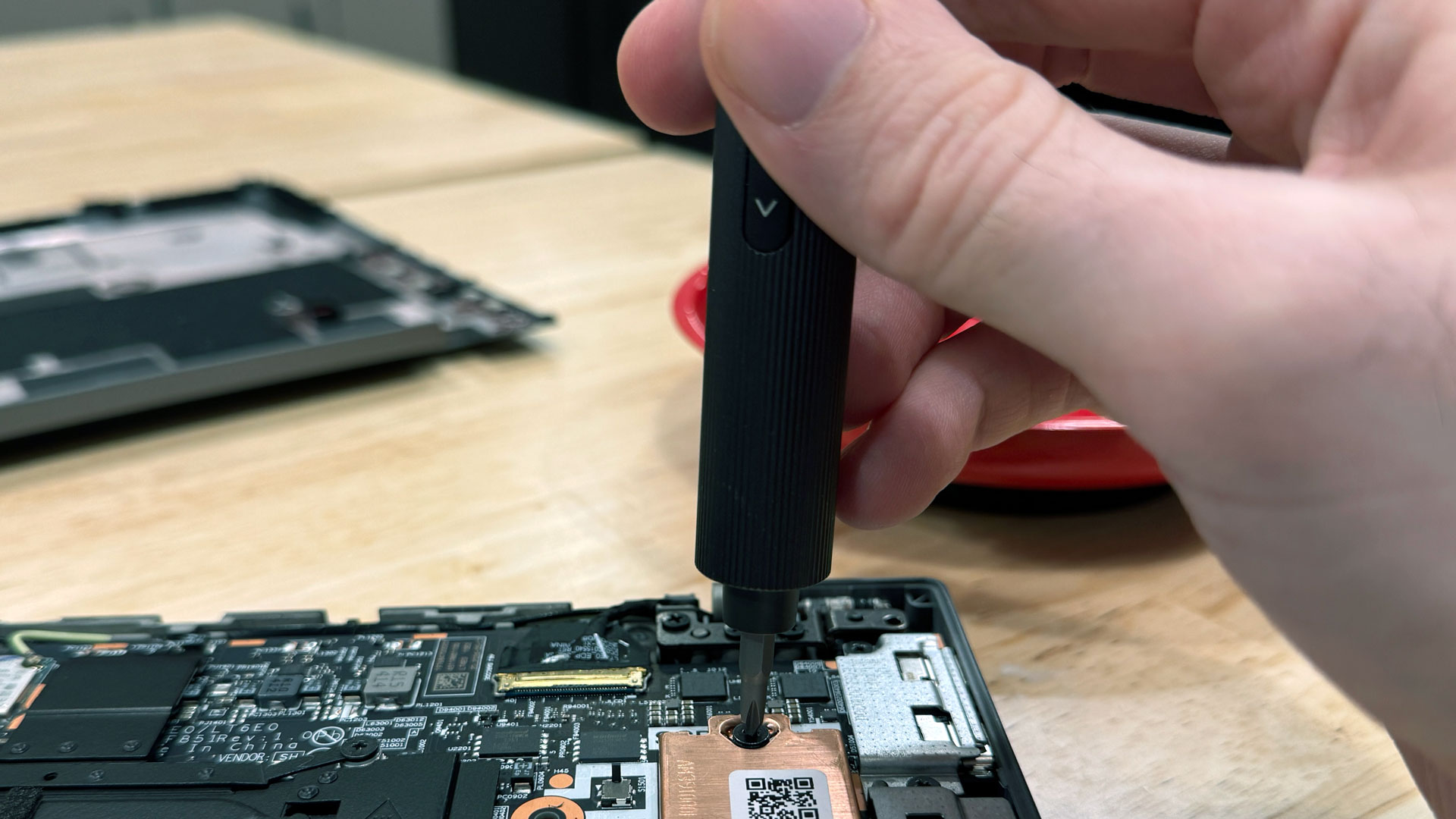 Hoto 25-in-1 screwdriver being used on a laptop on a wooden workbench.