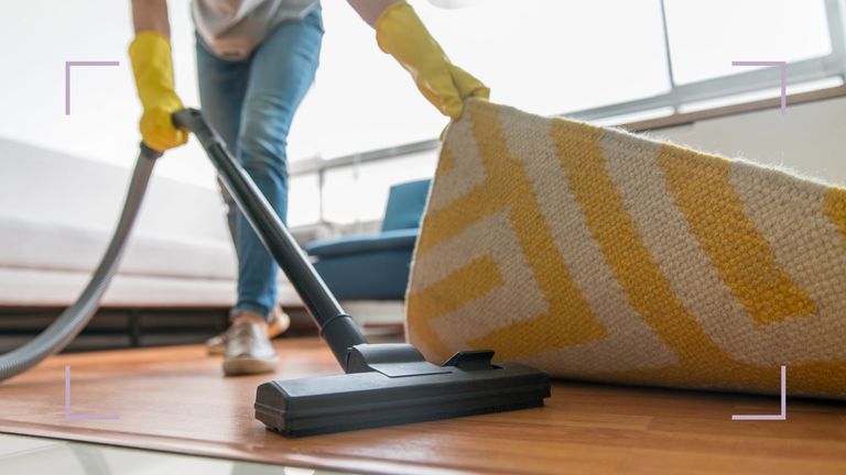 Person vacuuming wooden floor under the rug to support article by experts on how often should you vacuum