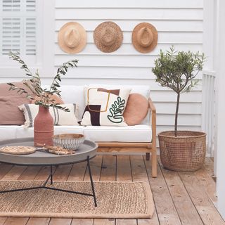 Scandi-inspired outdoor living room with white sofa, rattan rug and hats hanging on wall.