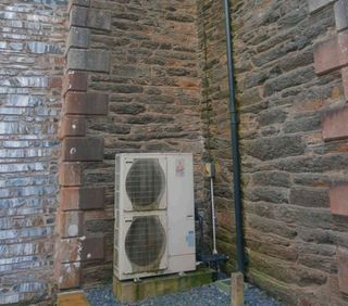 A heat pump in an old building against a brick wall