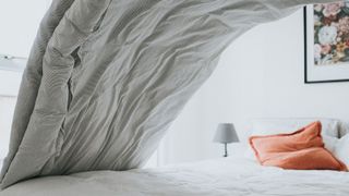 Grey duvet cover being placed on top of white bed sheet