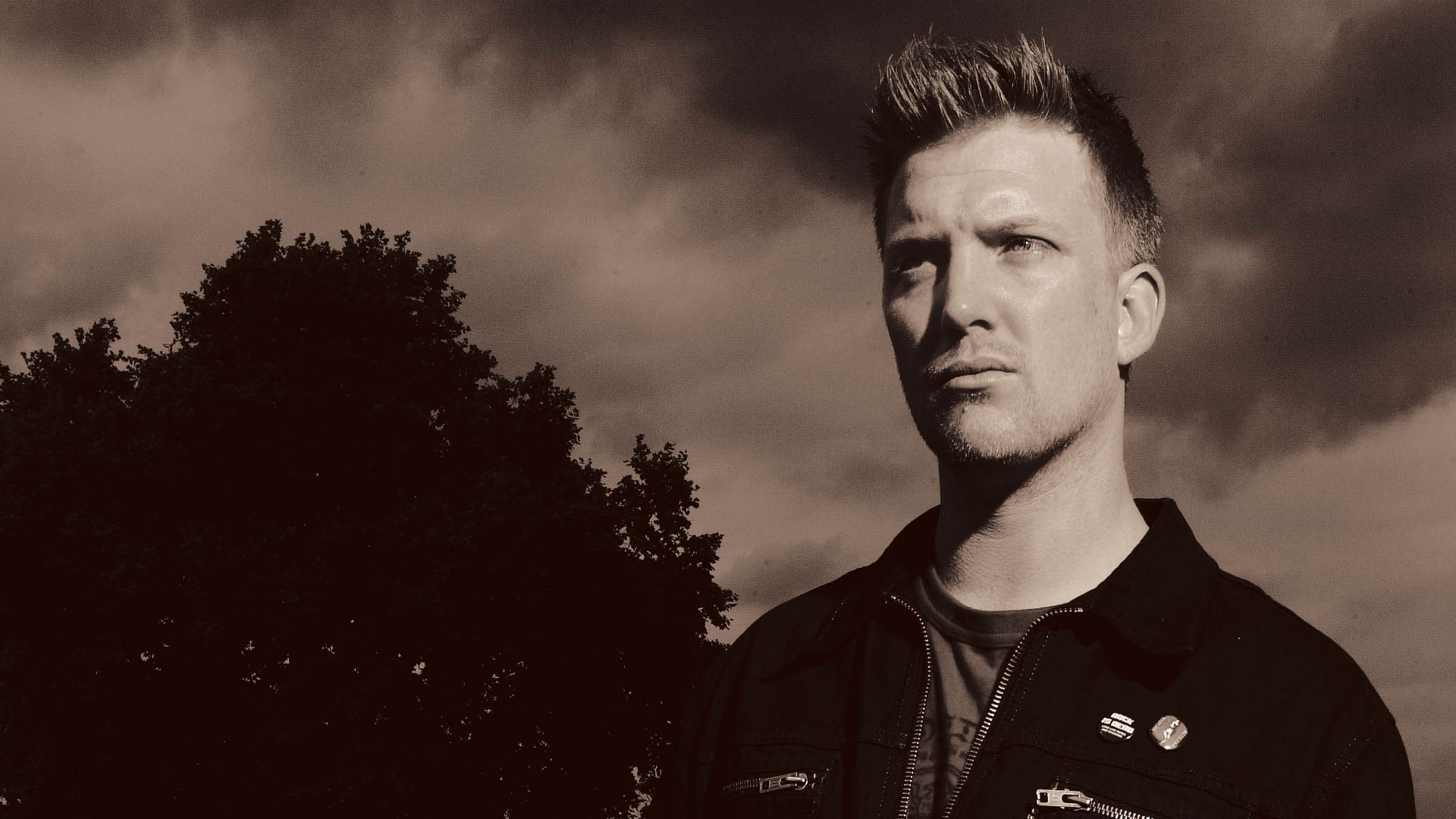 A sepia portrait of Josh Homme in a field next to a tree