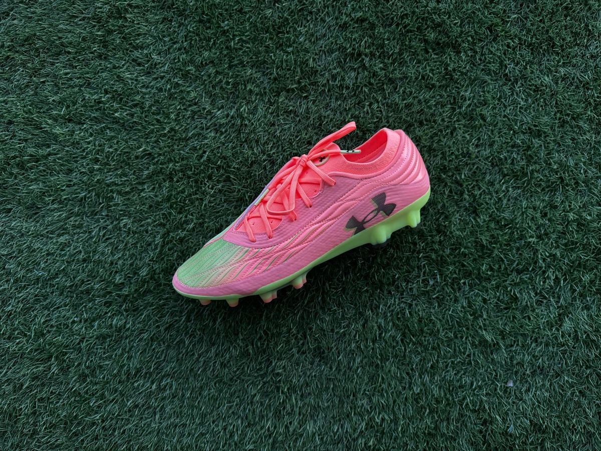 Under Armour Clone Magnetico Elite 4.0 football boots A bird&#039;s eye view of pink and green football boots with pink laces and the Under Armour logo on the sole, sitting on green artificial grass. 