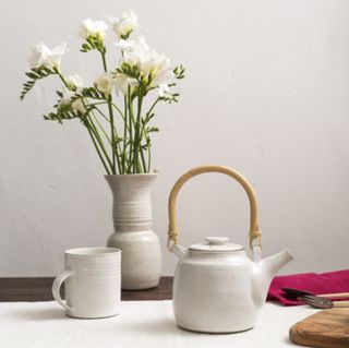 tea kettle with cups and flower vase and white wall
