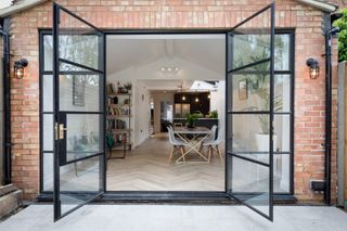 A modern home extension with red bricks and open glass doors leading into an open plan dining room and kitchen