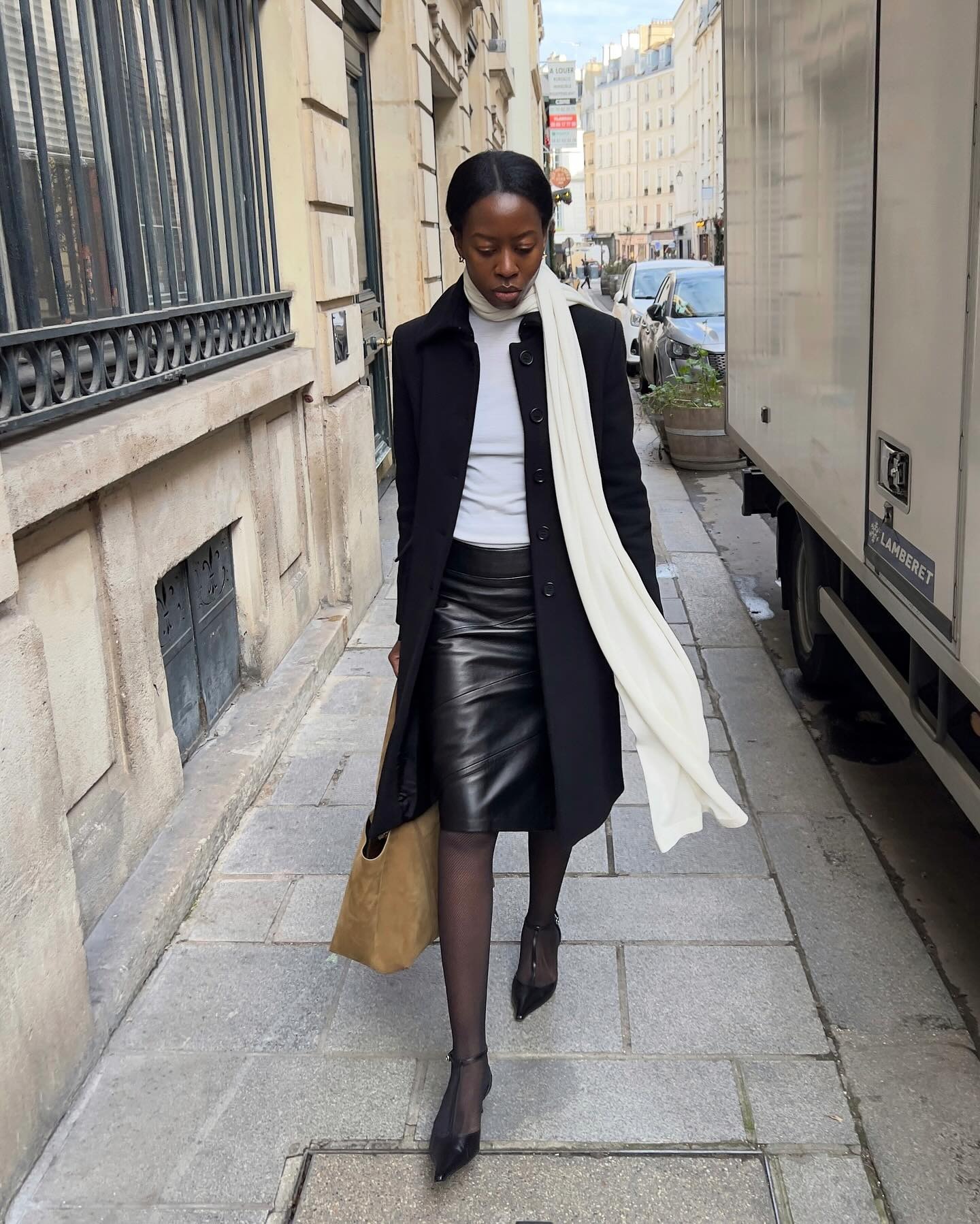 French influencer @sylviemus_ wears a black leather knee-length pencil skirt with a white top, black coat and long cream scarf.