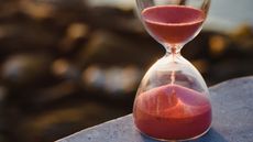 Red sand flows through an hourglass.