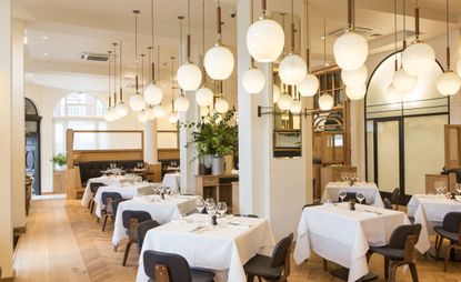In the Modern Pantry Clerkenwell, there is a black chair and table with white clothes and a gorgeous ceiling hanging