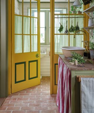 kitchen/pantry with terracotta tiles, sink, fabric skirt/curtain, shelving, herbs, yellow door and windows