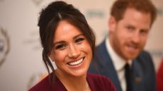 A close up of Meghan Markle with Prince Harry in the background