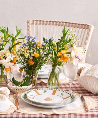 An outdoor dining table with a red and white striped tablecloth and orange and blue floral arrangements in vases