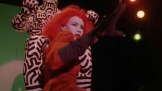 Grace Jones holds up a clawed hand in mid-performance in Vamp.