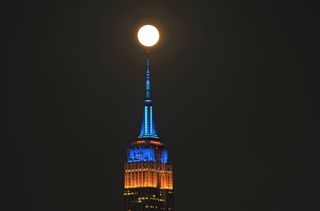 a bright moon in the sky above a tall skyscraper colored blue and yellow by lights