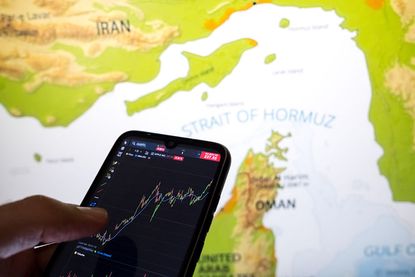A stock chart on a smartphone screen with a map of the Strait of Hormuz