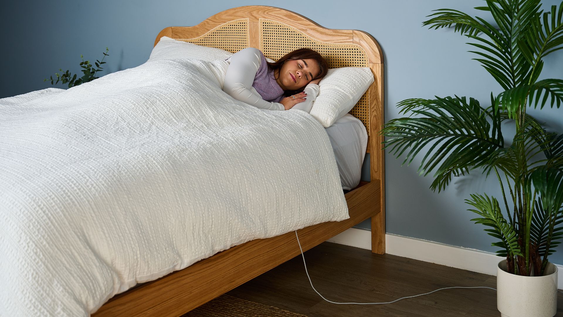 Tom's Guide's sleep tech tester in bed with white sheets on wooden bed frame testing the Withings Sleep Analyzer in sleep studio