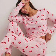 A woman wearing light pink pyjamas with heart shaped cherries on from Boux Avenue.
