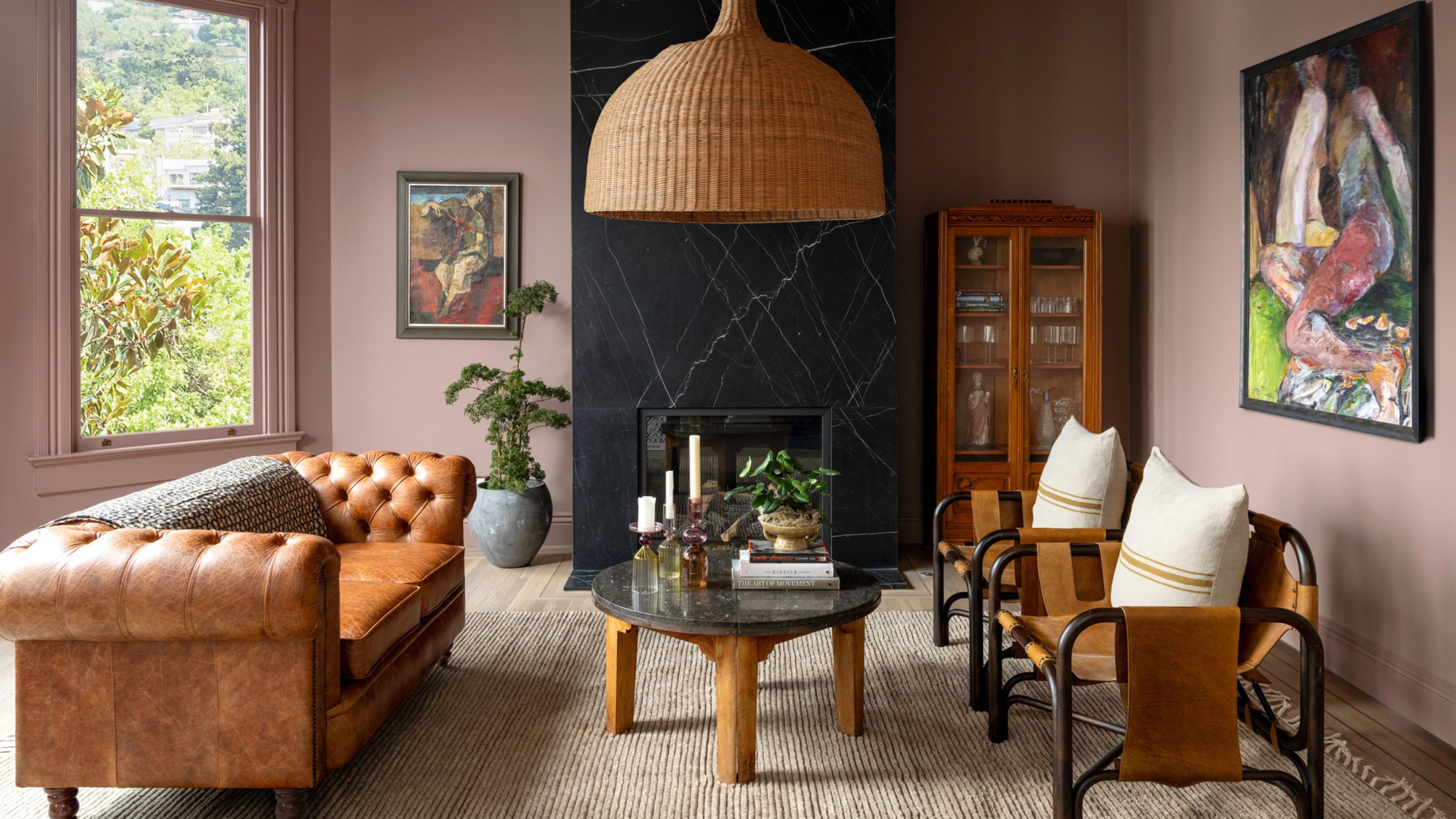 pink living room with black marble fireplace, rattan lampshade, brown chesterfield sofa, timber coffee table, beige rug and tan leather armchairs