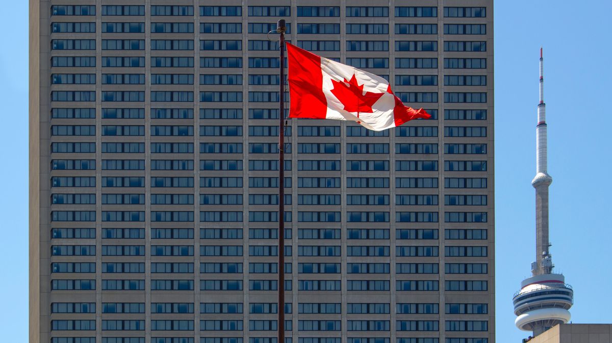 A Canadian flag, flying on a tall pole in front of a skyscraper.