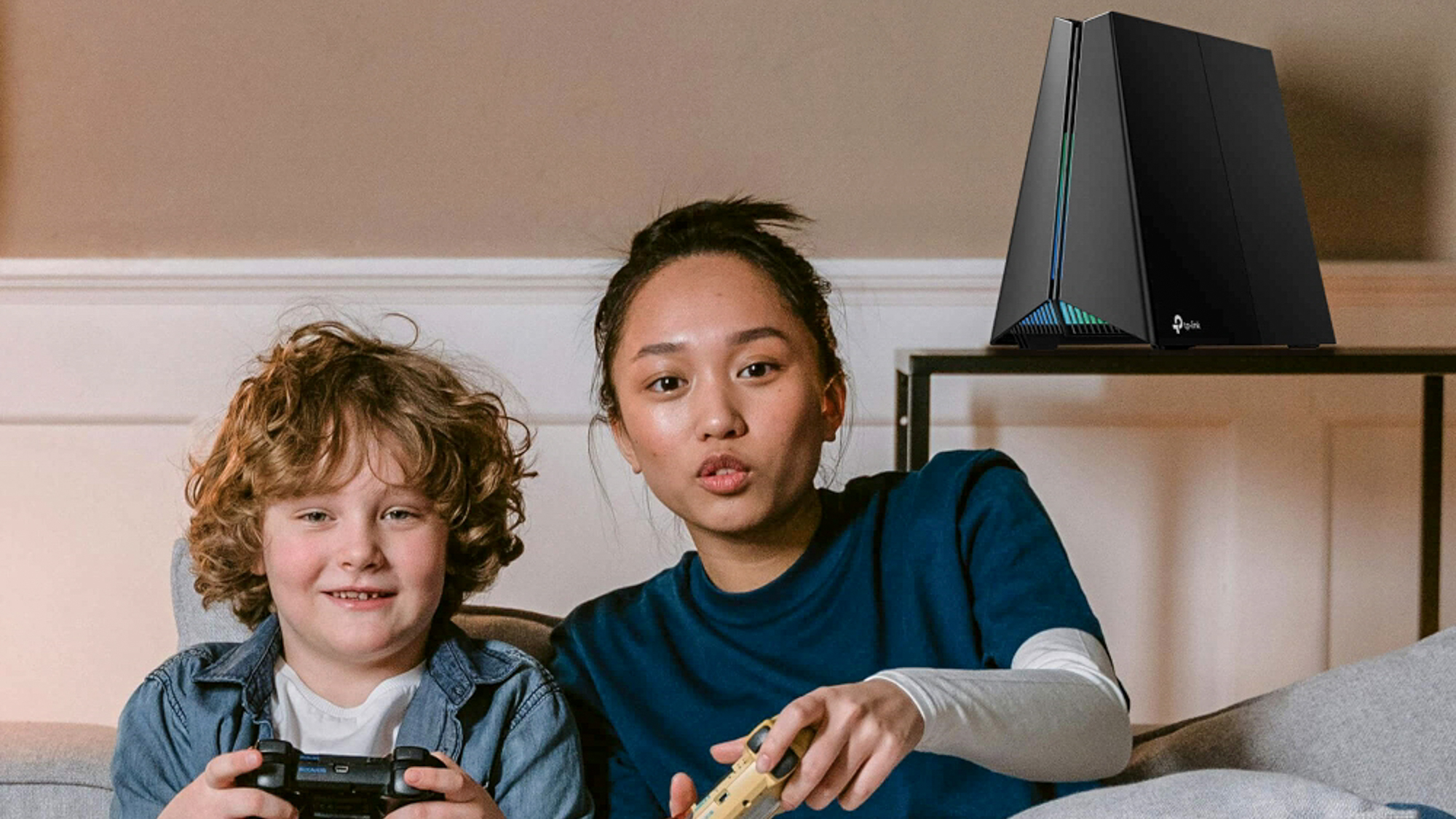 Two kids gaming next to a TP-Link Archer GE650 router