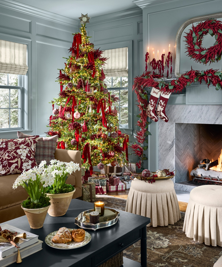 Opulently decorated Christmas tree dressed in plumes of burgundy amaranthus, tassels, and mercury glass, inside of a sky-blue-living room filled with wrapped presents and antique-inspired accents