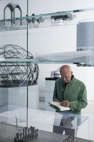portrait of norman foster writing something down in front of models
