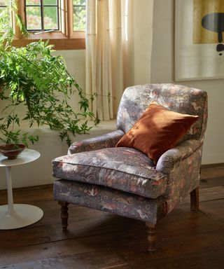 Bright entryway with dark wooden flooring, crittal windows, cream curtains and an upholstered armchair with animal designs on gray, with orange cushion. It's bright, airy and feels like spring