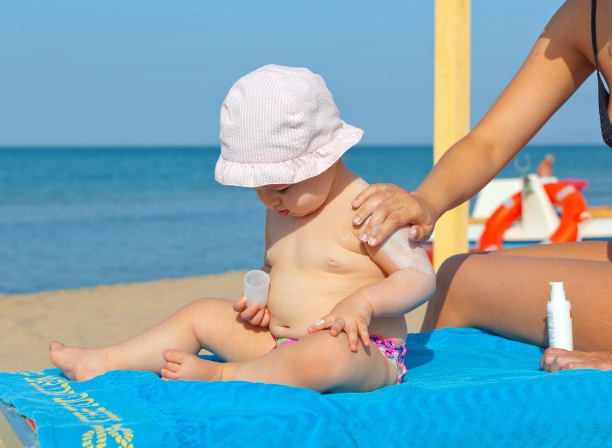 Adult putting sunscreen on a baby on the beach.