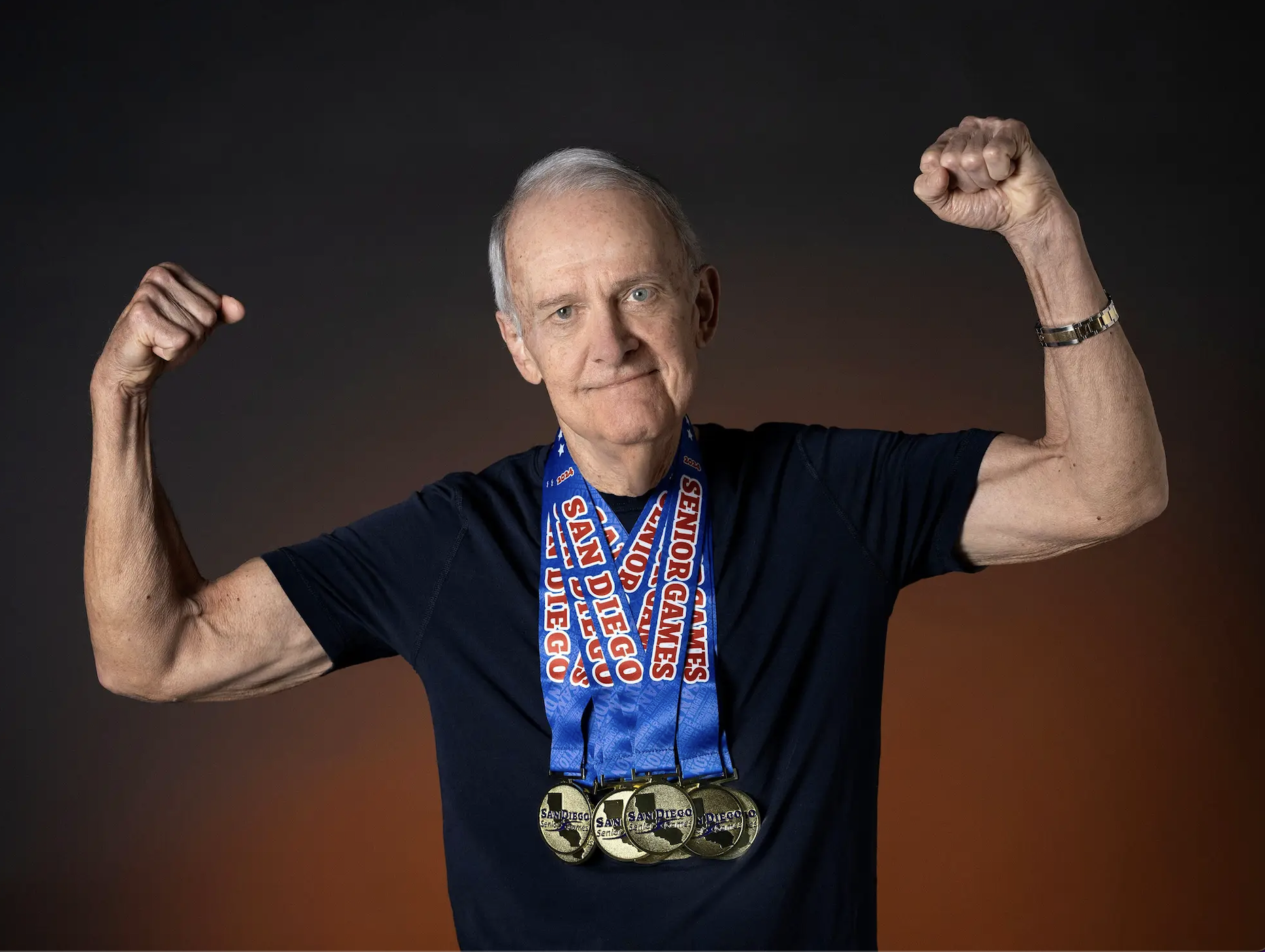 Senior man in biceps flexing pose, wearing multiple gold medals with