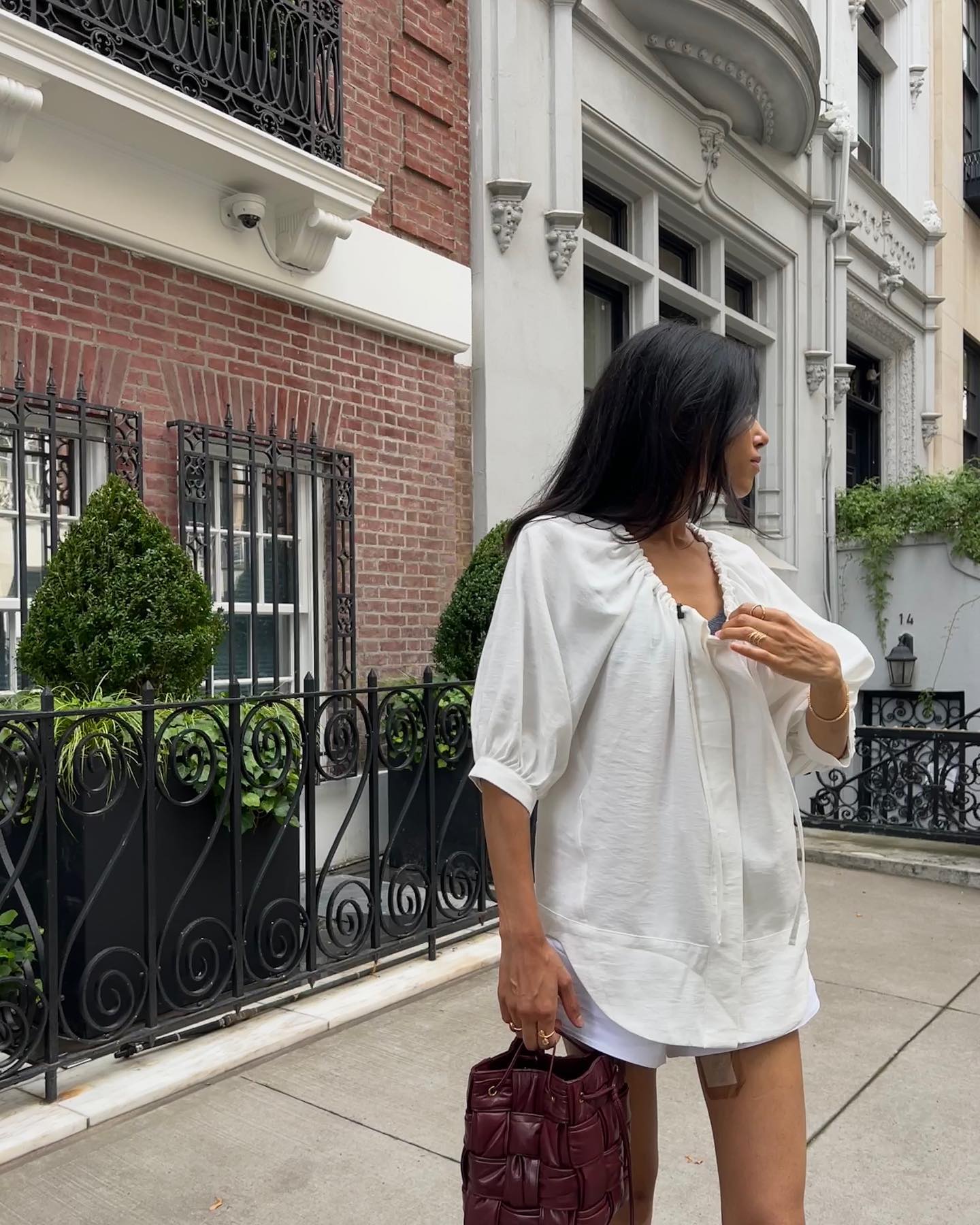 @shayinjune wearing a white blouse, white drawstring shorts, and a burgundy leather bag.