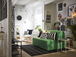 open plan living space with green sofa, shelving unit, gallery wall, armchair, pendant, floor lamps, rug