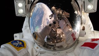 an astronaut in a spacesuit. you can see his gloved hands taking a picture in the reflection from his helmet. also in the reflection is earth and a strut of the international space station