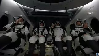 The four astronauts of SpaceX's Crew-2 mission for NASA wave to a camera as they prepare to exit the capsule after a successful splashdown off the coast of Pensacola, Florida at night on Nov. 8, 2021.