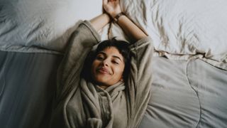 Woman lying on her back in bed stretching and smiling