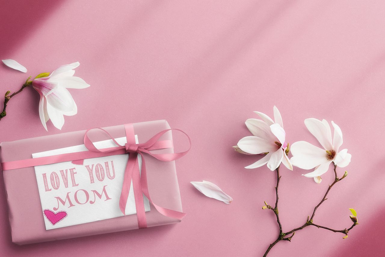 a pink gift parcel that says I love you mom, next to flowers on a pink background 