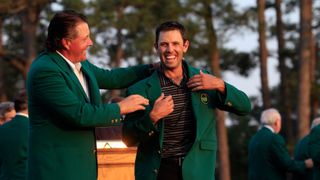Masters champion Phil Mickelson of the United States helps 2011 Masters Tournament winner Charl Schwartzel of South Africa at the Green Jacket ceremony after the final round of the 2011 Masters Tournament at Augusta National Golf Club