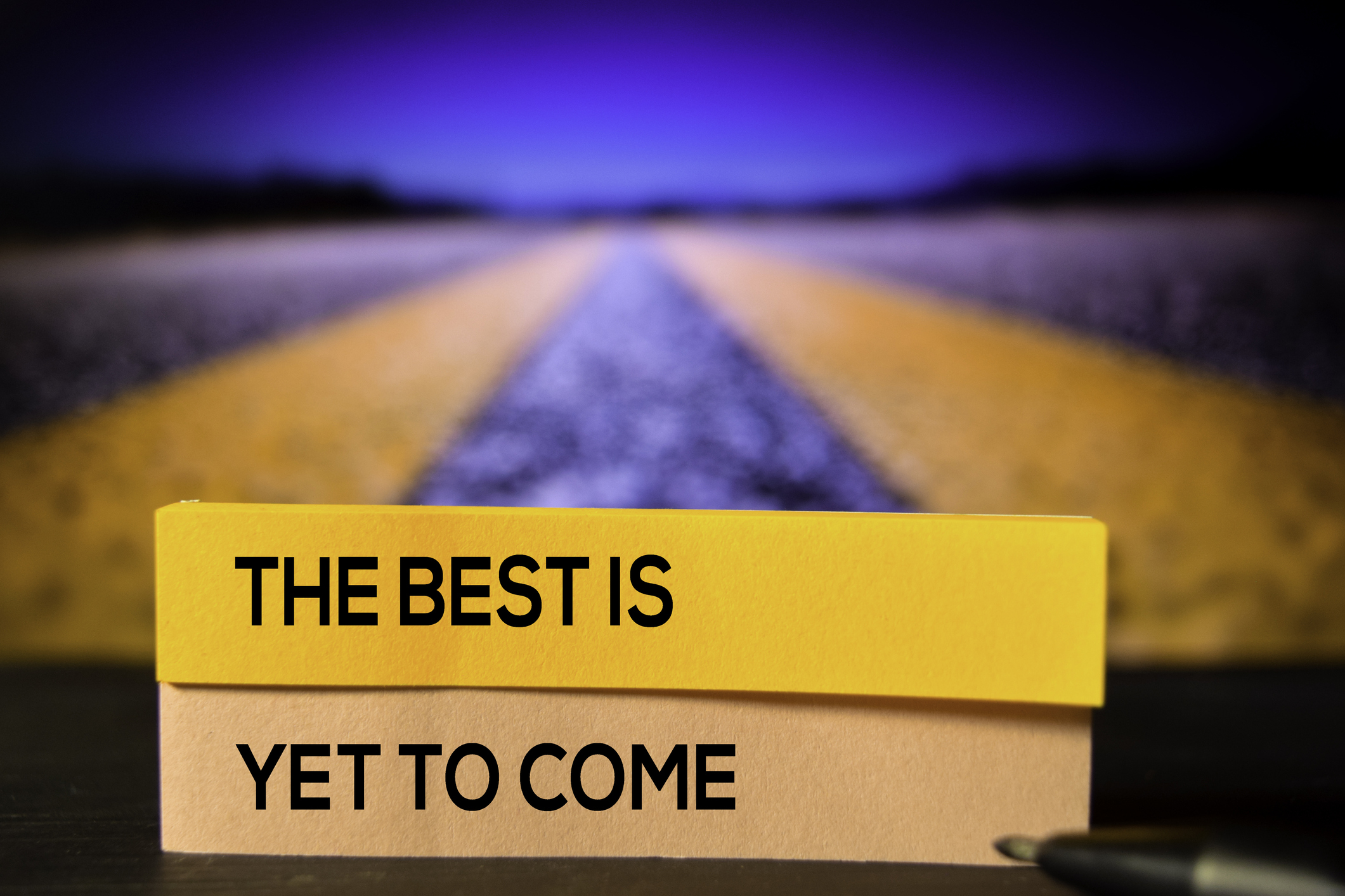 A road in the background with yellow lines to the distance, and small post-its saying "The best is yet to come" in block letters.