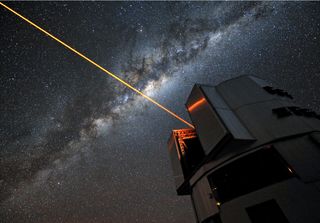 A bright laser beam shines out of the top of a telescope.