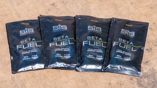Four sachets of SIS Beta Fuel Isotonic energy drink on a paved floor